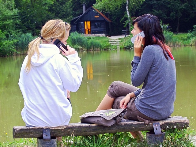 two women talking on cell phones on bench in nature